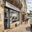 Une image photoréaliste générée par Gemini montre une scène de rue animée à Saumur, en France, avec le château de Saumur en arrière-plan. Au premier plan, on voit une façade de bâtiment historique en pierre abritant une entreprise locale de téléphonie VoIP appelée 'LA TÉLÉPHONIE DU SAUMUROIS'. Des employés utilisent des headsets et des softphones pour passer des appels VoIP depuis des ordinateurs portables et des smartphones, tandis qu'une plaque moderne affiche le titre de l'article sur la téléphonie VoIP pour les PME et les commerces locaux. Des câbles de fibre optique sont visibles le long de la façade du bâtiment, symbolisant la connectivité. Des gens marchent dans la rue pavée et une camionnette de livraison électrique de 'GAIA CLOUD' est garée à proximité. L'image capture la fusion entre l'architecture historique de Saumur et la technologie de pointe de la téléphonie VoIP.